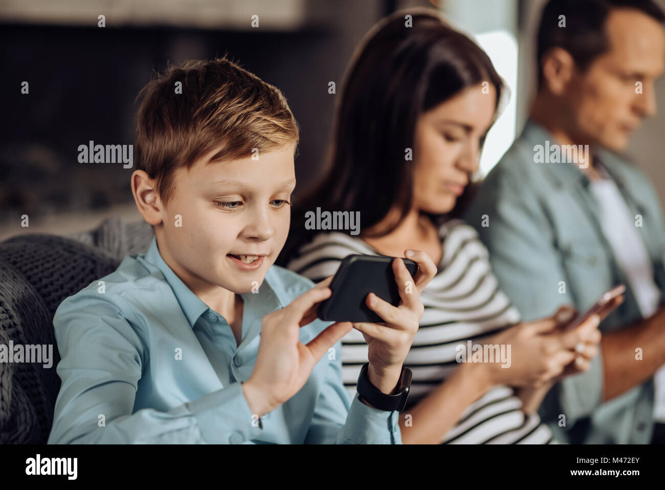 Pre-teen boy riproduzione su telefono accanto ai suoi genitori Foto Stock