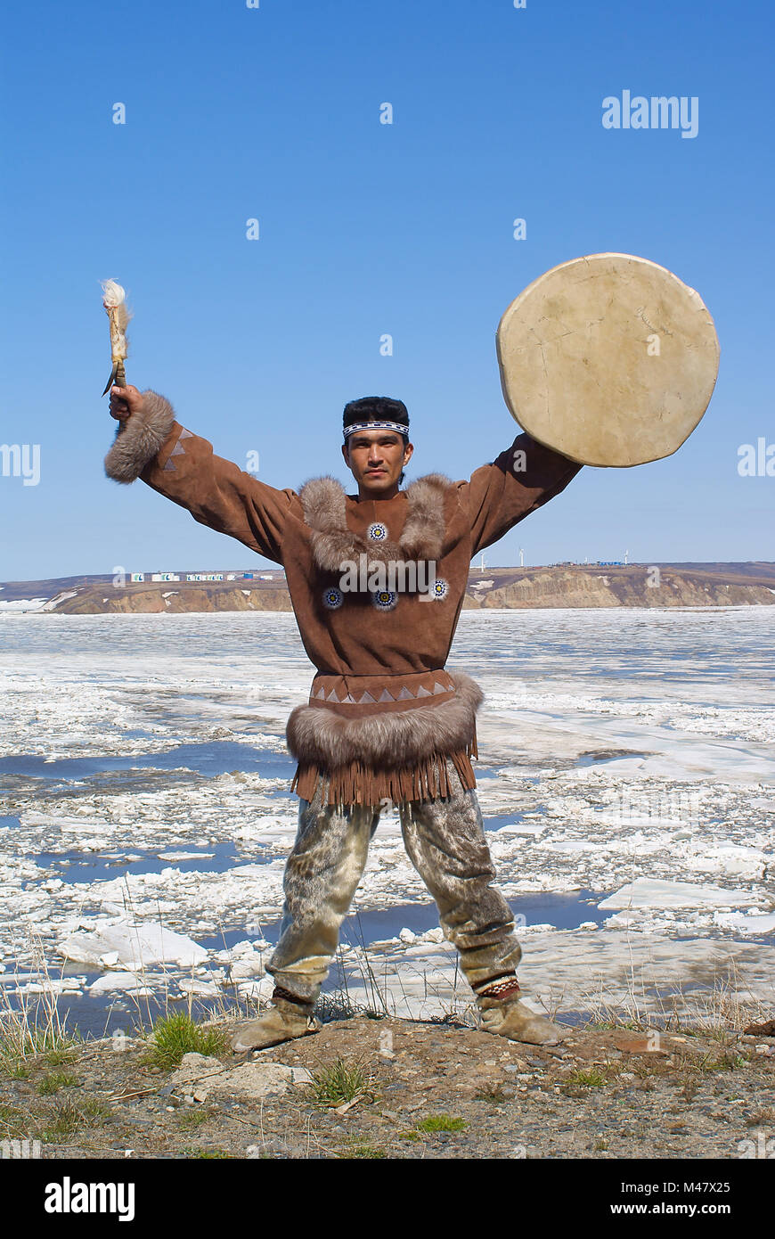 Chukchi uomo in abiti tradizionali è un ballo folk dance con il tamburello e la spinge contro la molla a Chukotka paesaggio Foto Stock