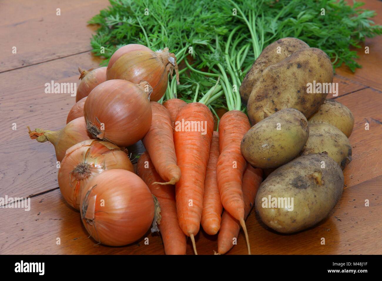 Cipolle, carote e patate su una cucina in legno tavolo. Foto Stock