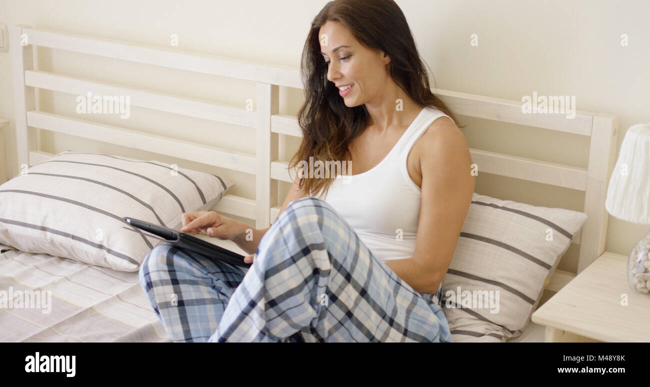 Giovane donna seduta sul suo letto tramite un tablet Foto Stock
