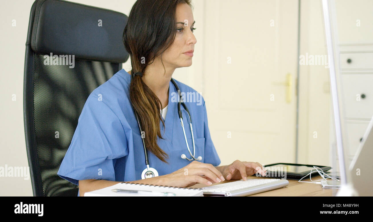 Giovane medico donna seduta digitando nel suo ufficio Foto Stock