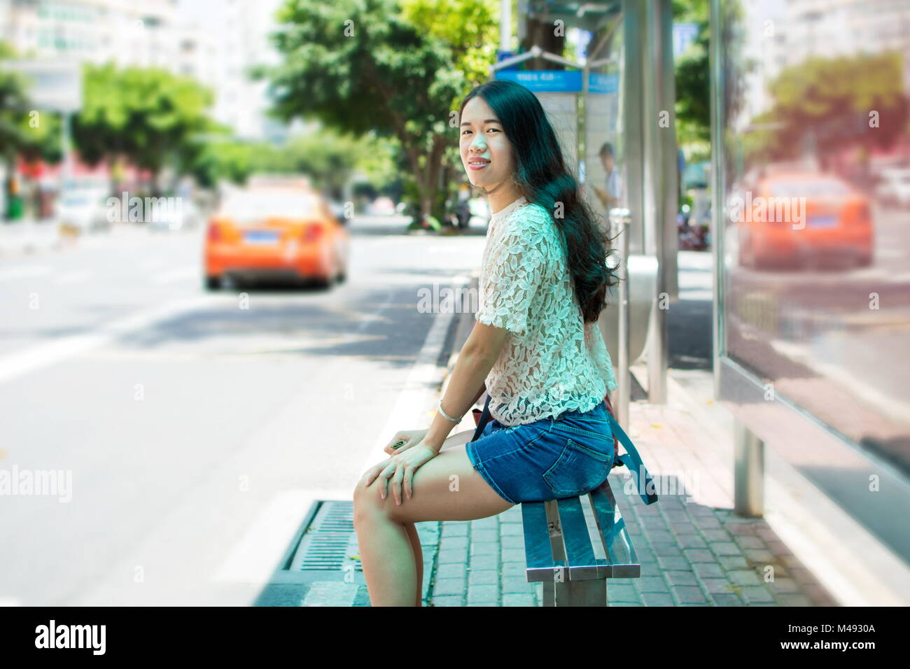 Ragazza di attesa per i mezzi di trasporto pubblici presso la fermata degli autobus Foto Stock