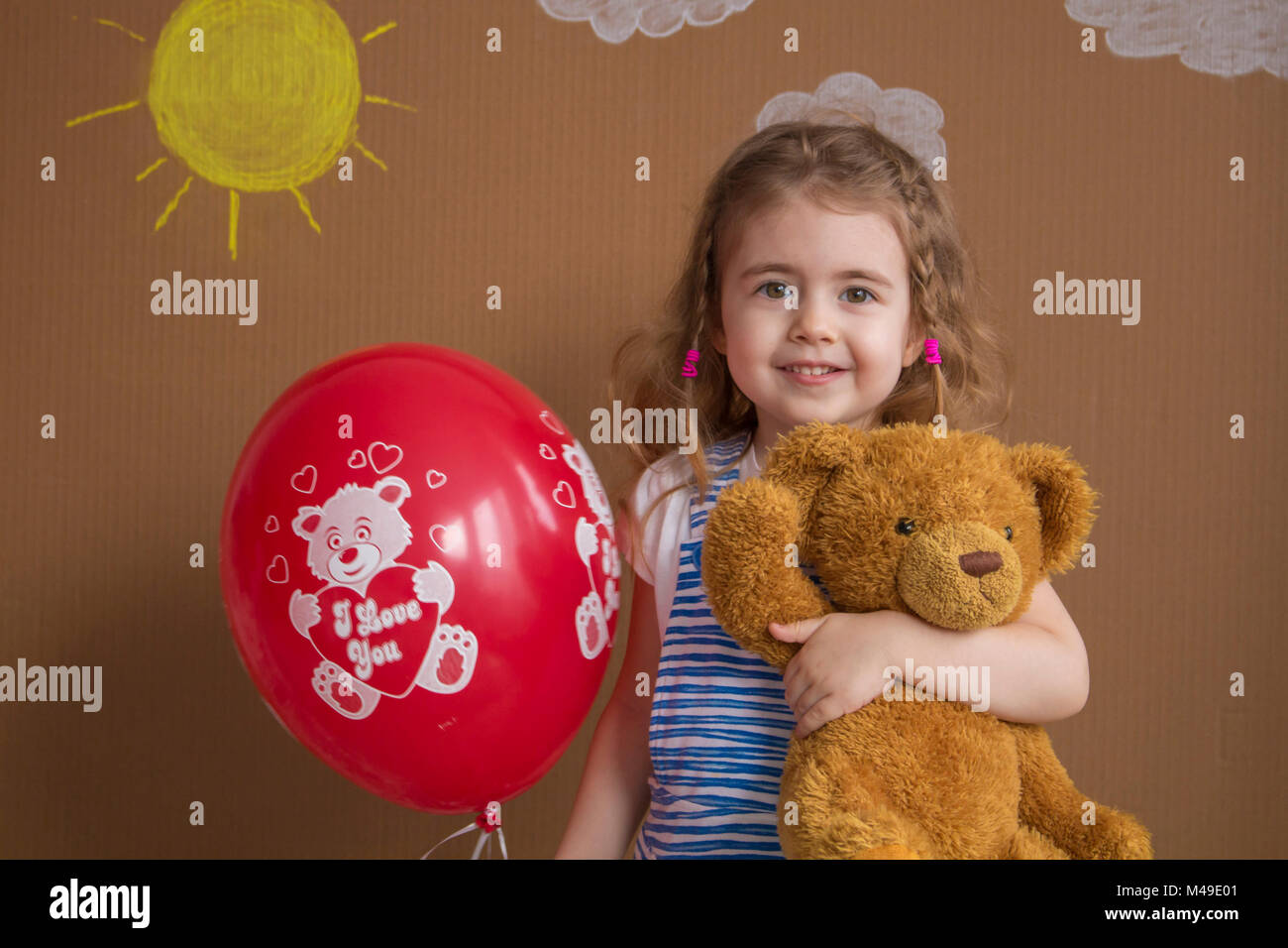 Ragazza carina con Teddy bear holding palloncino rosso, sorridente alla fotocamera. Foto Stock