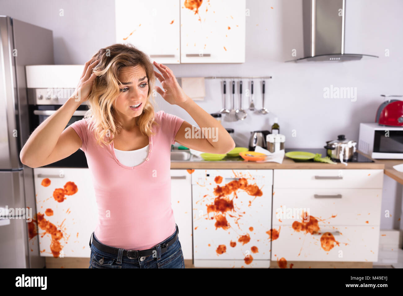 Ritratto di un preoccupato giovane donna in piedi sporchi la cucina di casa Foto Stock