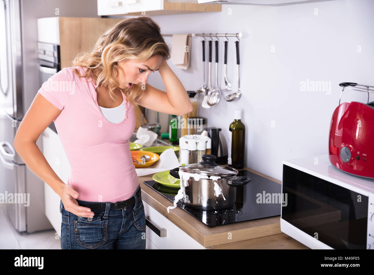 Scioccato giovane donna guardando la fuoriuscita di latte bollito dall'arnese di cucina Foto Stock