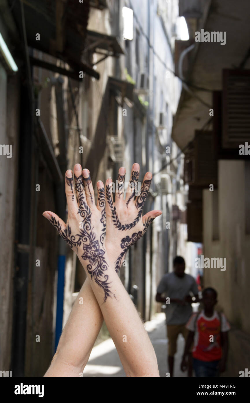 Donna di henna decorate mani giunte in posizione verticale in un vicolo in Stone Town, Zanzibar, Tanzania in una luminosa e soleggiata giornata Foto Stock