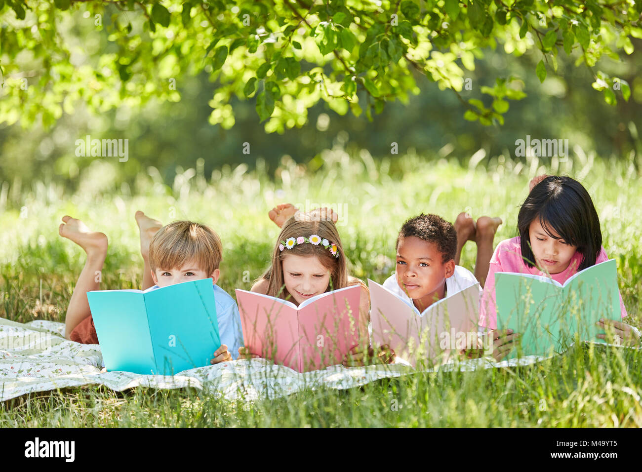 Gruppo multiculturale dei bambini la lettura mentre studiava nel parco in estate Foto Stock