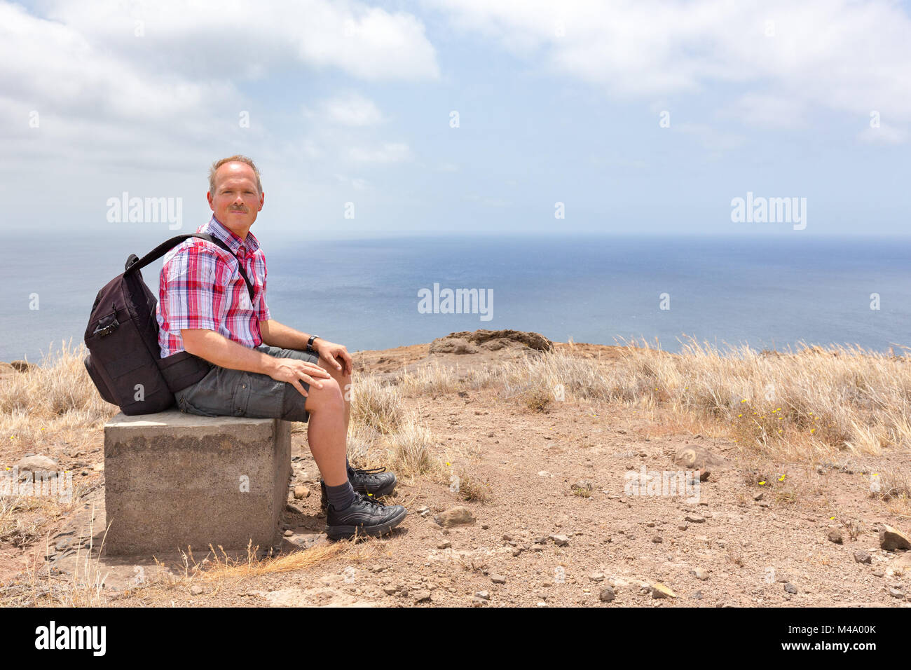 Uomo con zaino seduta in salita a costa del mare Foto Stock