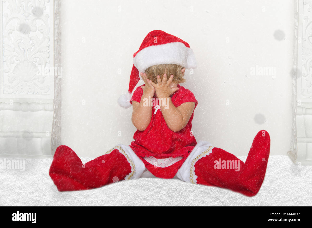 Bambino in Santa suit seduto sul pavimento con la neve Foto Stock