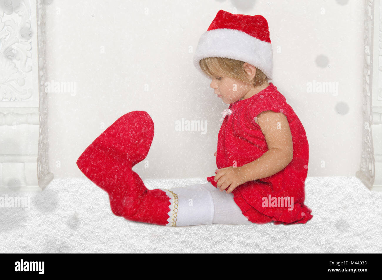 Un bambino piccolo a Santa suit seduto sul pavimento con la neve Foto Stock