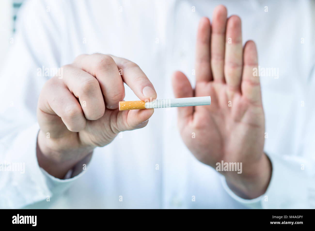 Medico dice di smettere di fumare. Azienda sigaretta tra le dita e che mostra un segno di stop con la mano. Foto Stock