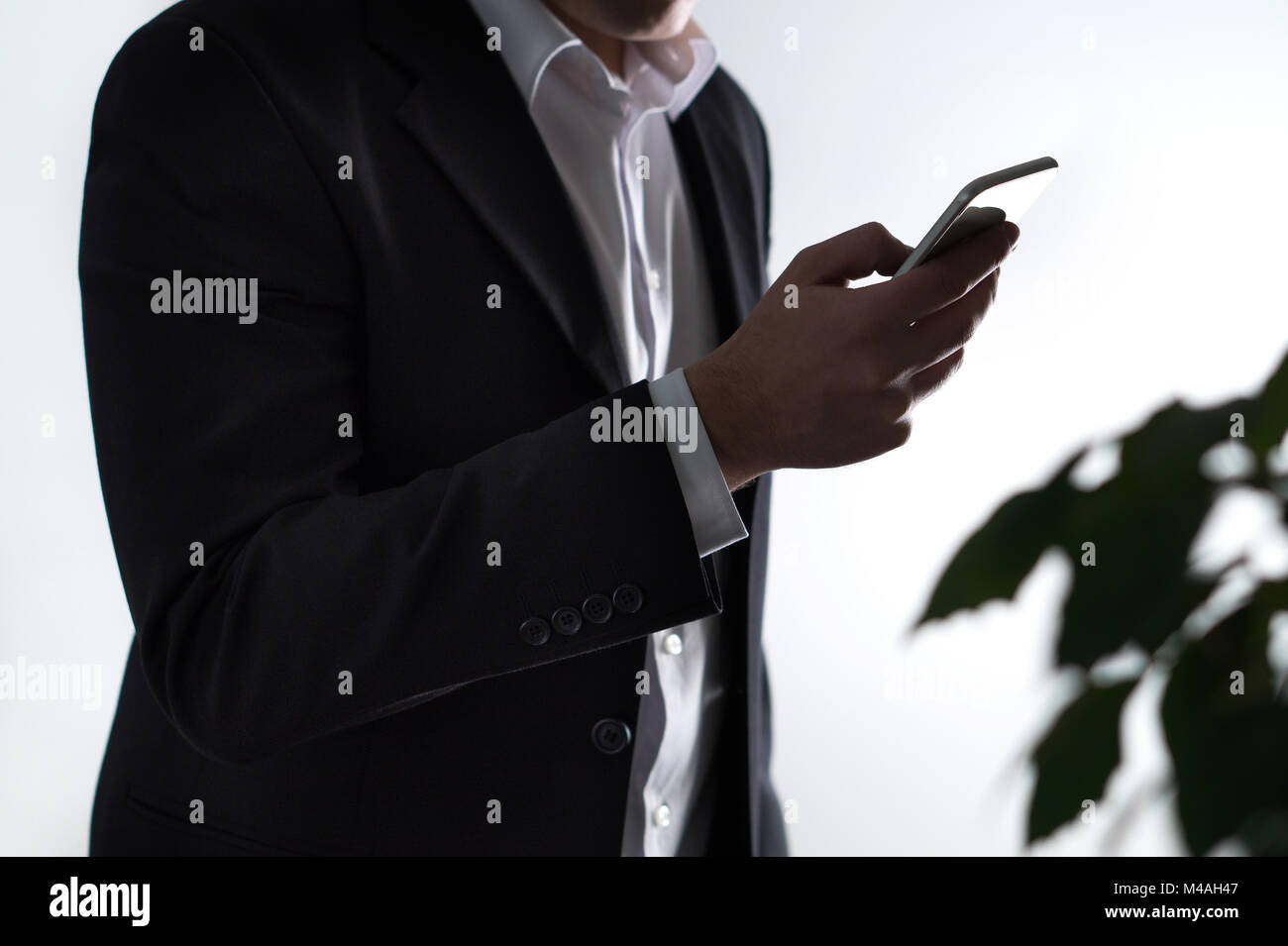 La sicurezza mobile, phisning e crimini online. Imprenditore o un uomo in una tuta tenendo lo smartphone in ombra scura. Le frodi finanziarie con smart device. Foto Stock