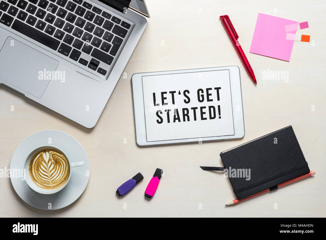 Iniziamo la scrittura su schermo di tablet con laptop, notebook e caffè giacente su legno scrivania in ufficio come laici piatta Foto Stock