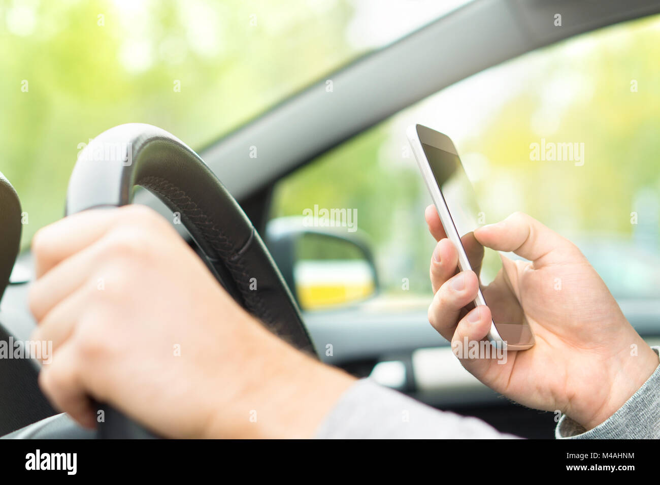 Uomo che utilizza smartphone durante la guida. Driver sms e l'invio di sms e utilizzando il telefono cellulare in auto. La scrittura e la digitazione di messaggio con il cellulare nel veicolo Foto Stock