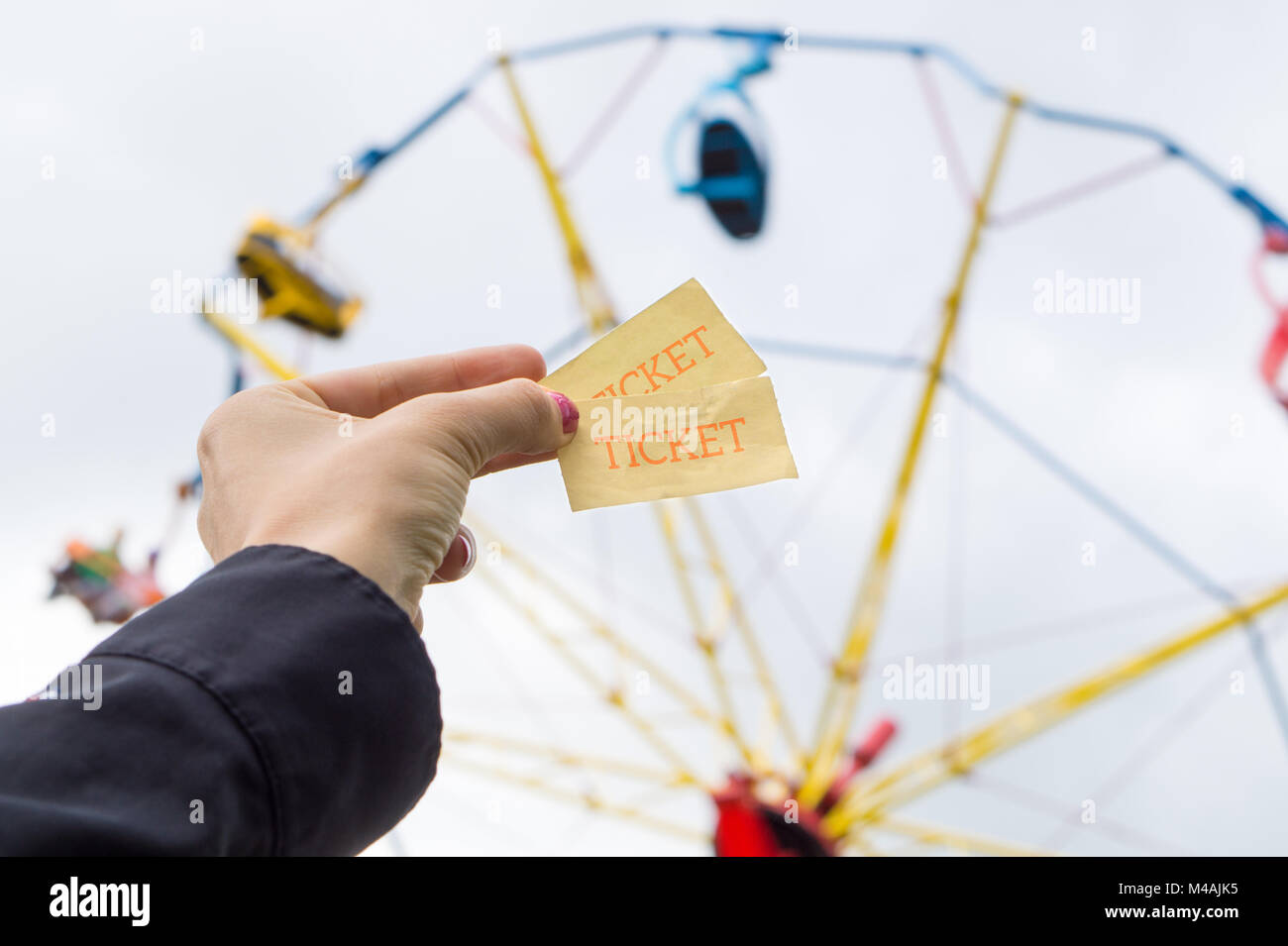 Ragazza o donna giovane azienda parco dei divertimenti di biglietti in mano. Colorato tema park ride in background. Foto Stock