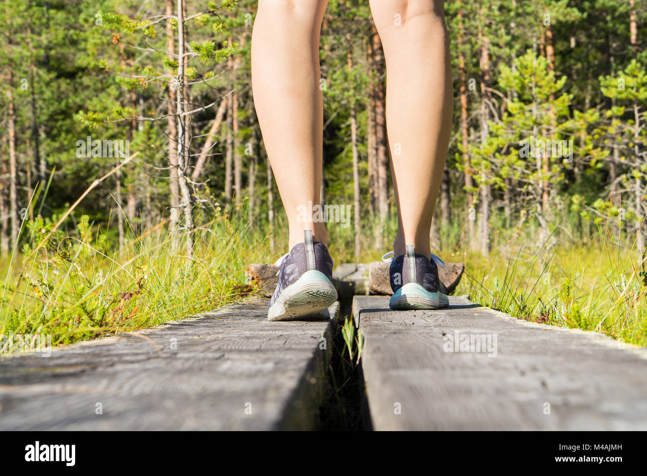 Giovani fitness sportivo donna in piedi sul graticcio in legno nella foresta. Vista posteriore di sneakers e gambe in boschi e natura verde. Uno stile di vita sano Foto Stock