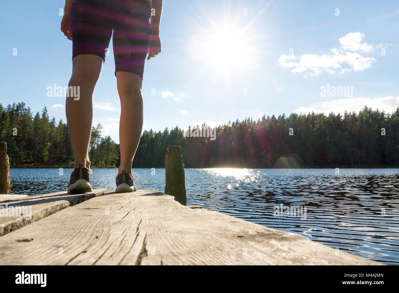 Giovane donna in piedi su un vecchio dock in legno e dal molo presso un lago in estate in Finlandia. Sole che splende in cielo blu. Tradizionale finlandese vista la natura. Foto Stock