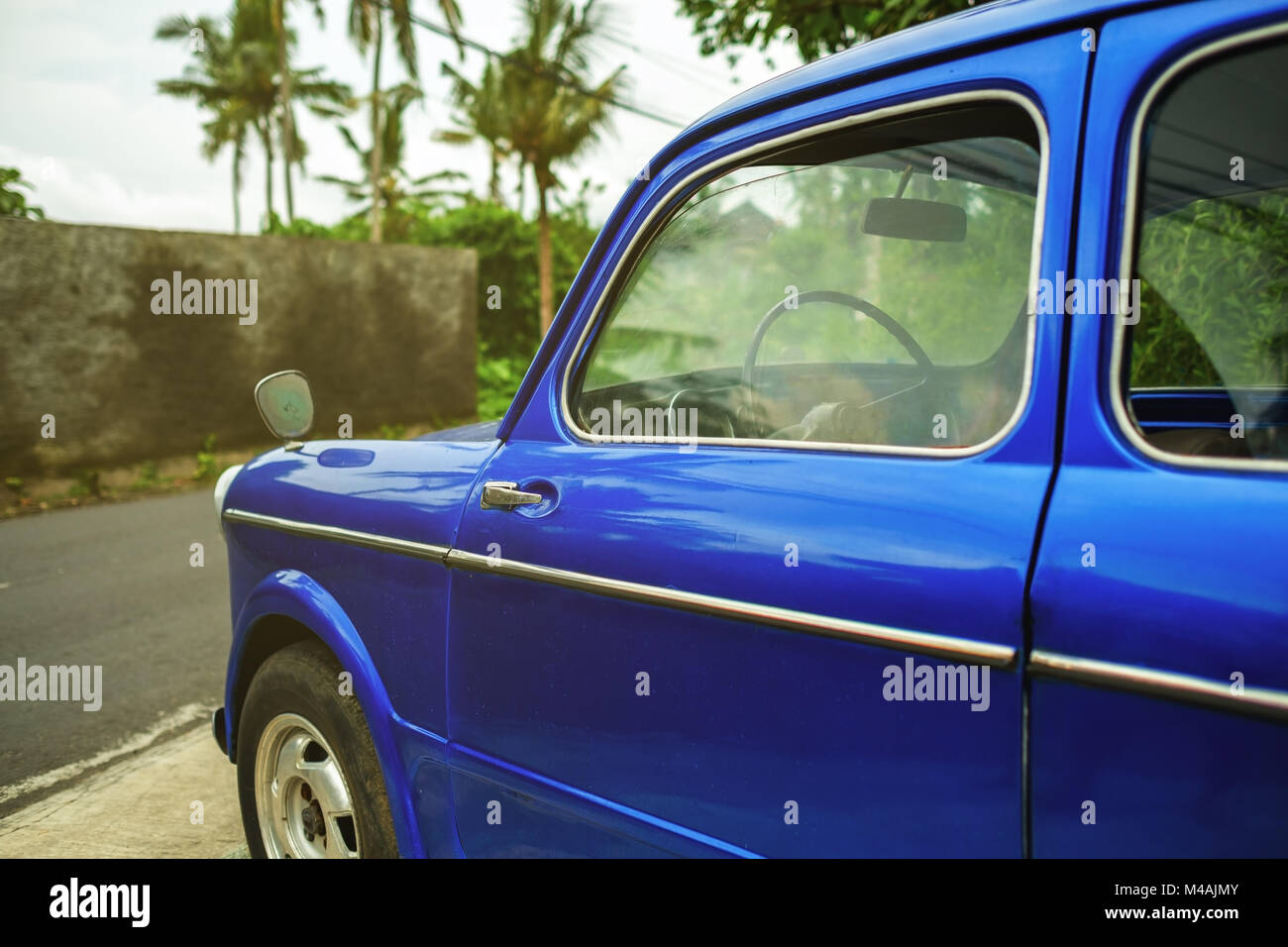 Vista laterale sul retro auto blu in città tropicale. Le palme sono su sfondo. Foto Stock