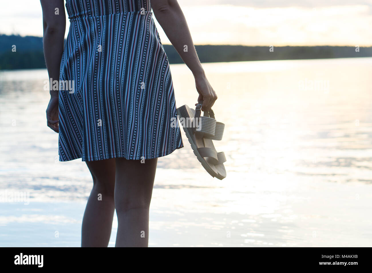 Donna nel vestire godendo bel tramonto sulla spiaggia. Libertà e stile di vita spensierata. Azienda di scarpe in mano. Foto Stock