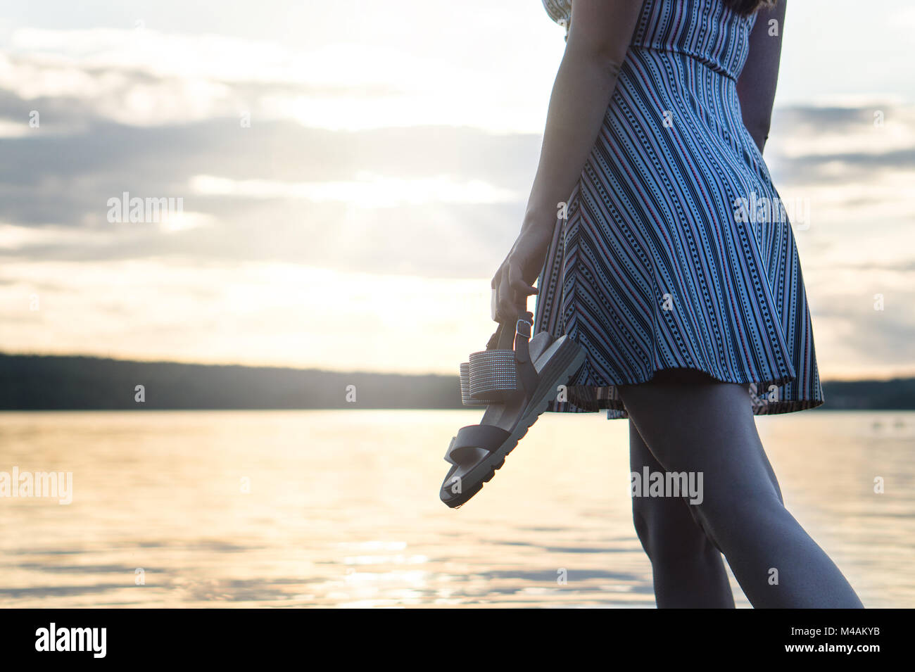 Coraggiosi e fiduciosi donna nel vestire godendo bel tramonto sulla spiaggia. Libertà e stile di vita spensierata. Azienda di scarpe in mano. Foto Stock