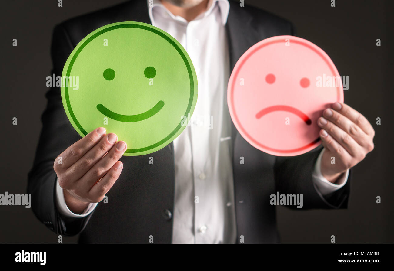 Uomo d affari con sorridenti e triste infelice carta cartone emoticon. Rating e dando recensione sulla soddisfazione del cliente o del team spi Foto Stock
