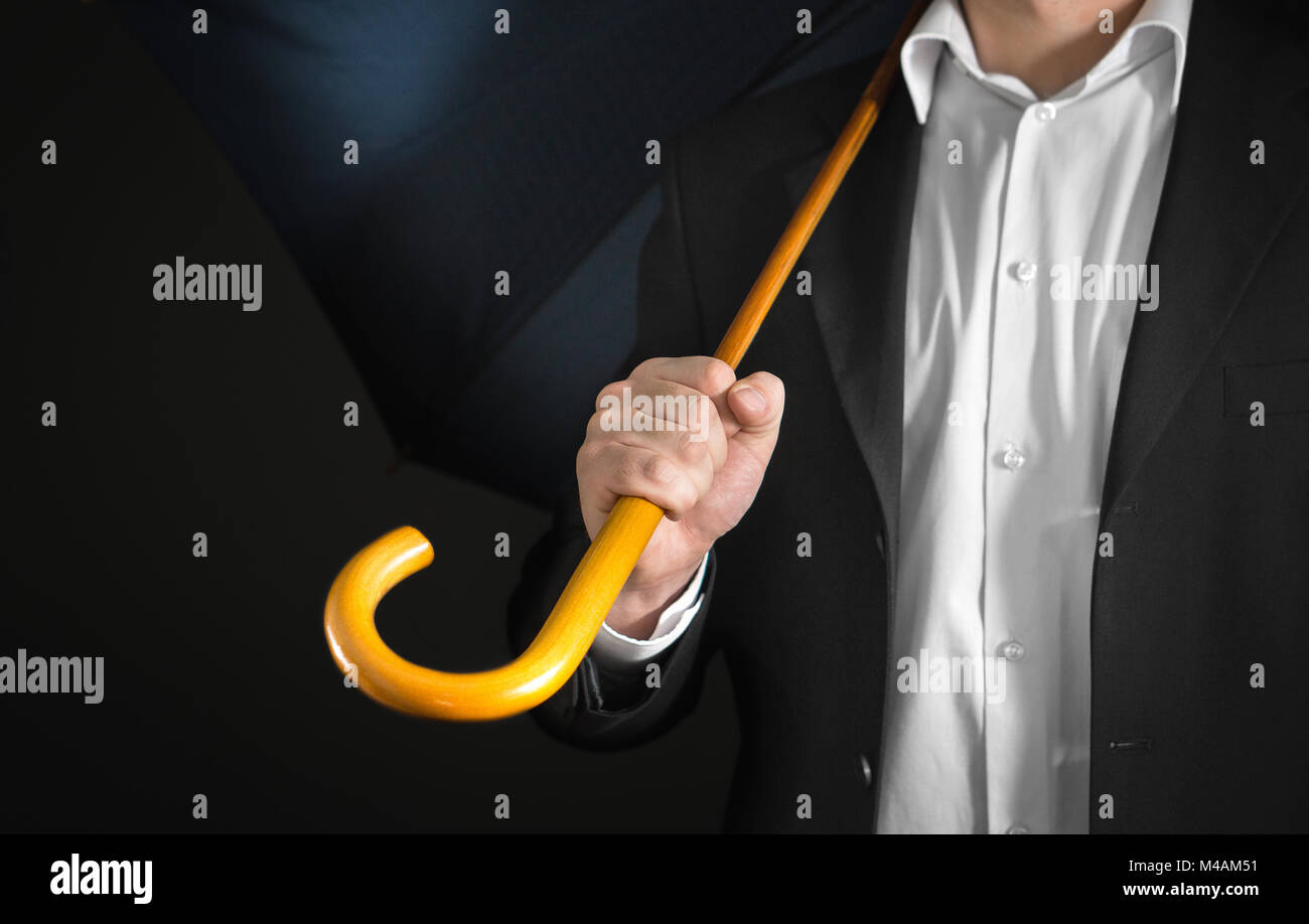 Business man holding ombrello con manico in legno sulla sua spalla con sfondo scuro. Triste la disoccupazione, guasto, fallimento, sul lavoro, bruciare e Foto Stock