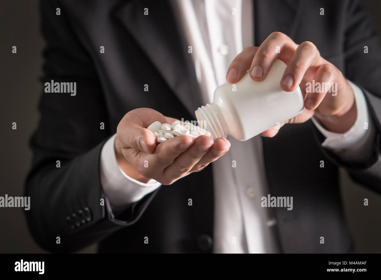 Rappresentante farmaceutica, consulente o testa direttore o manager della società di medicina con compresse di colore bianco. Uomo in una tuta versando la fuoriuscita di pillole. Foto Stock