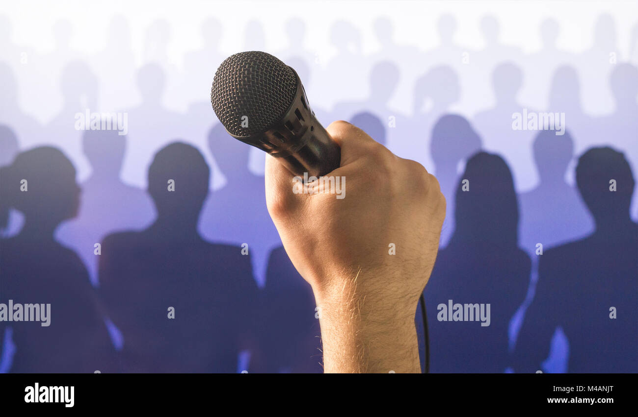 Parlare in pubblico e dare la parola concetto. Mano che tiene il microfono davanti a un pubblico di silhouette e la folla di gente. Il canto a microfono karaoke. Foto Stock