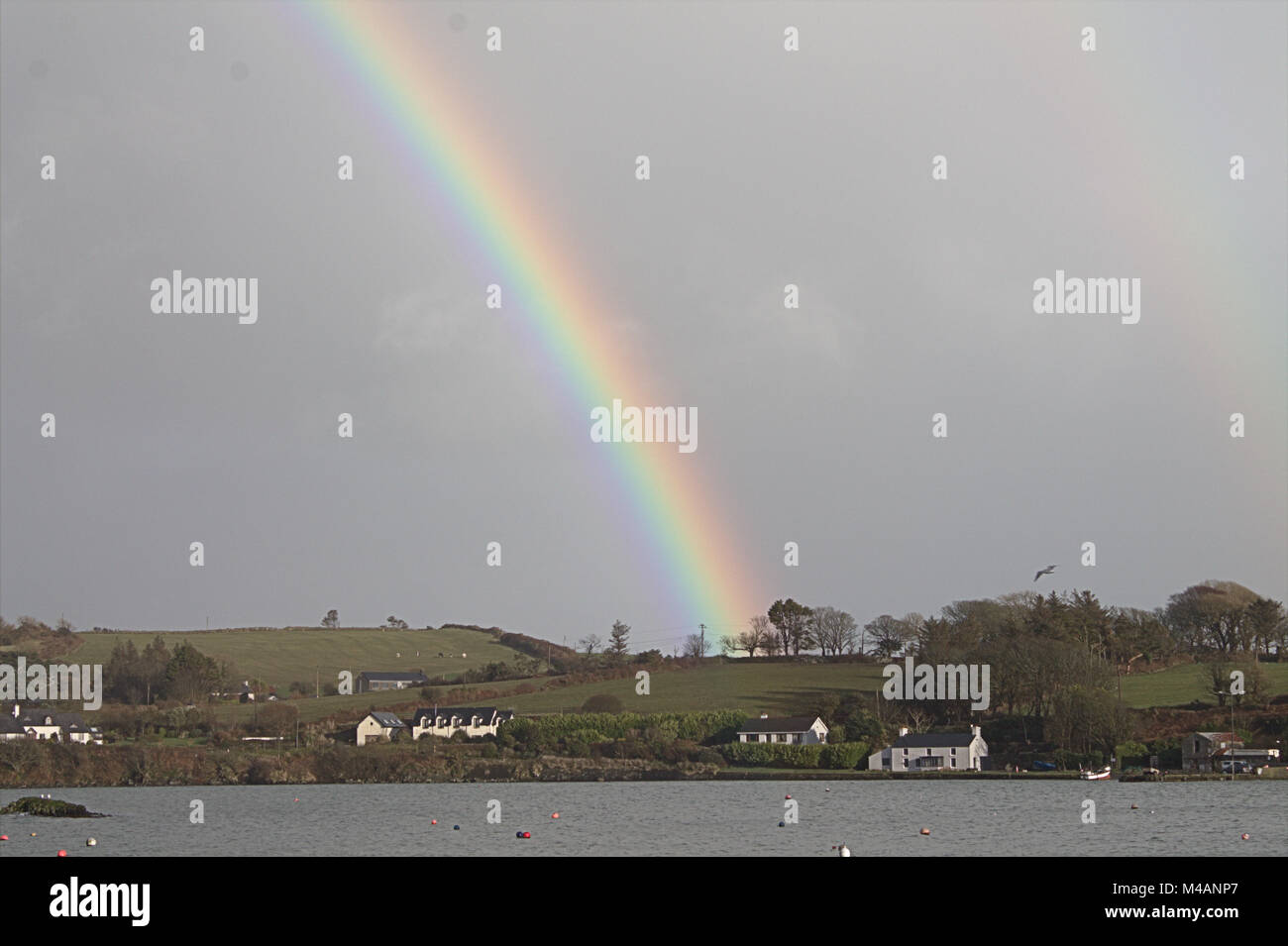 Rainbow che termina sul tetto di un cottage sulle rive di un estuario in West Cork, Irlanda Foto Stock