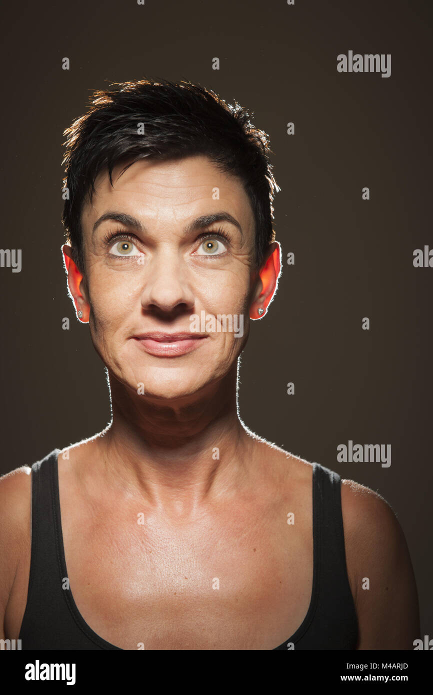 Sorridente dai capelli neri donna che guarda verso l'alto su nero Foto Stock