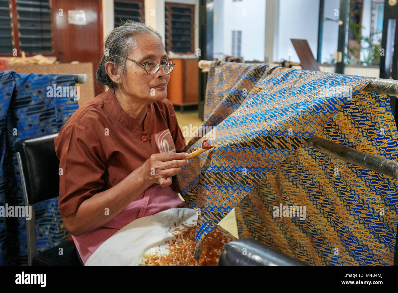 Craftswoman applicando cera calda-resistere tintura su batik con un canting sgorga (attrezzo). Il batik Winotosastro shop, Yogyakarta, Java, Indonesia. Foto Stock