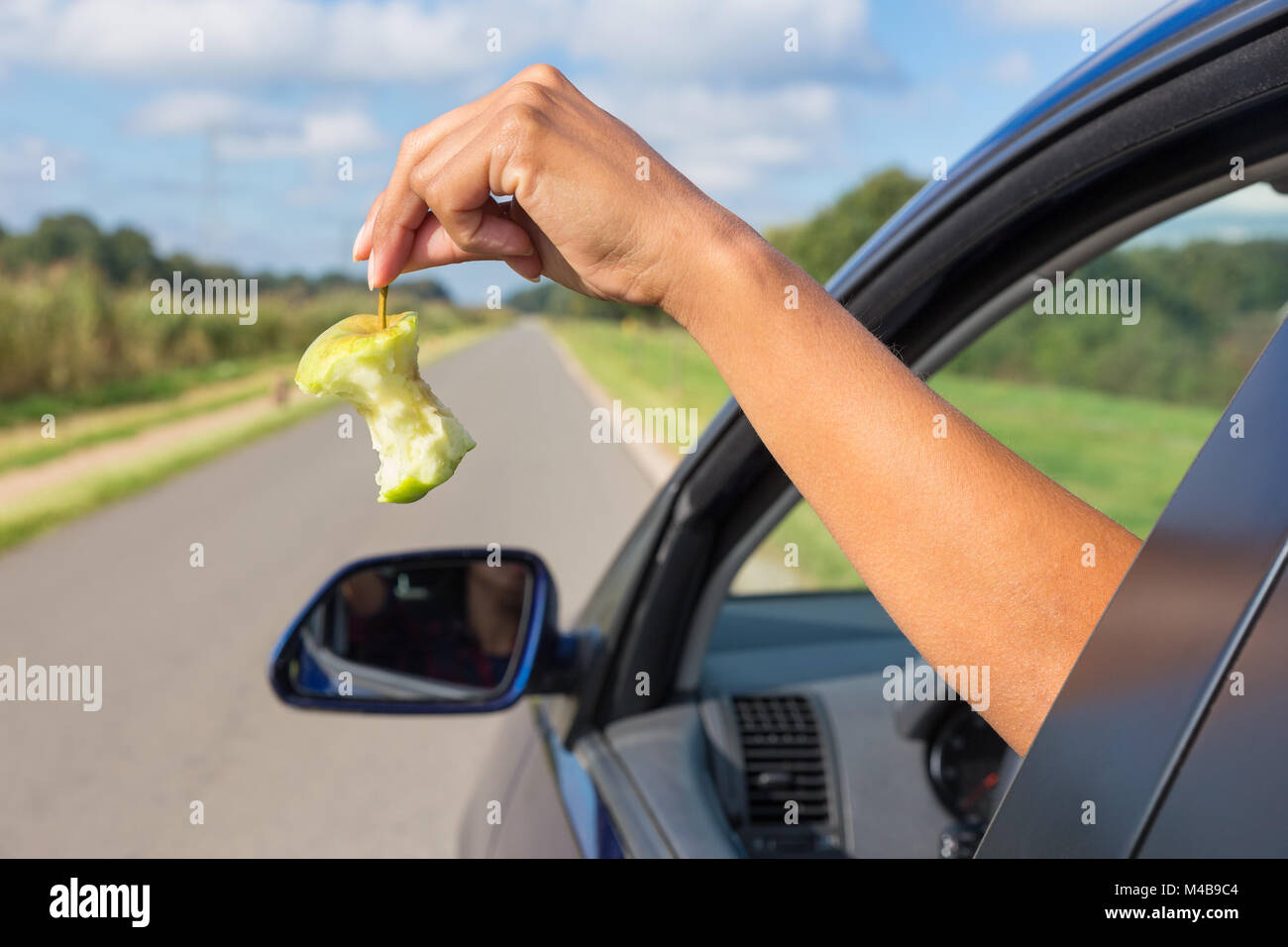 Braccio femmina la caduta di apple core fuori la finestra auto Foto Stock