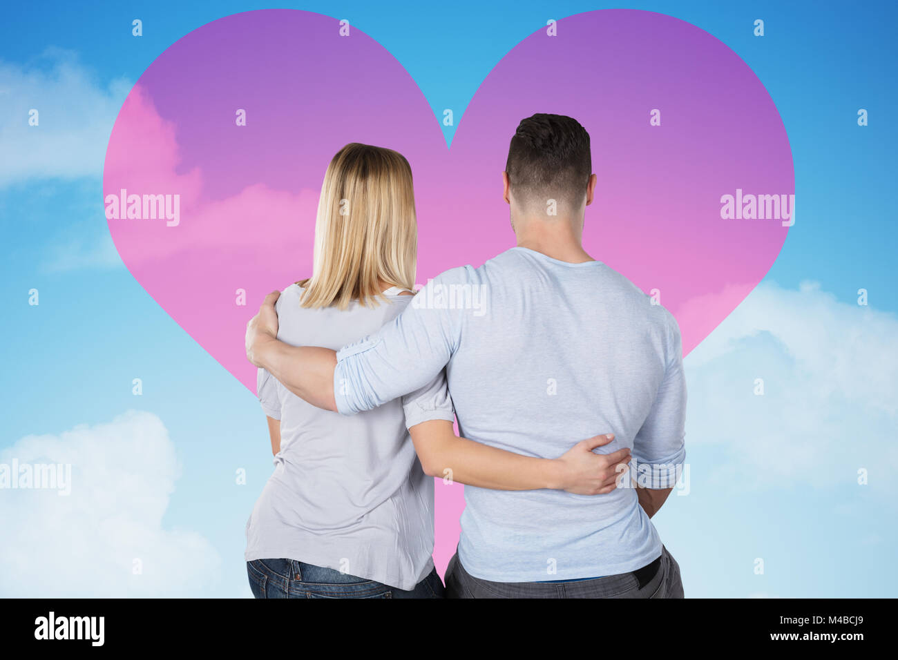 Vista posteriore di un amore giovane che guarda al cuore rosa su Sky Foto Stock