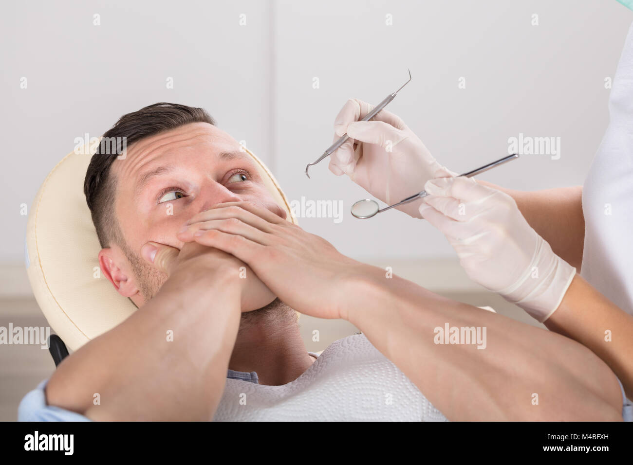 Uomo che copre la bocca con le mani mentre avente Dental Checkup in clinica Foto Stock