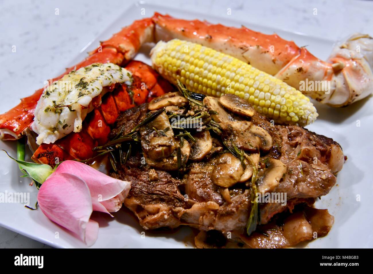 Bistecca, aragosta, granchio reale e un lato di sulla pannocchia di mais accompagnati da un unica rosa Foto Stock