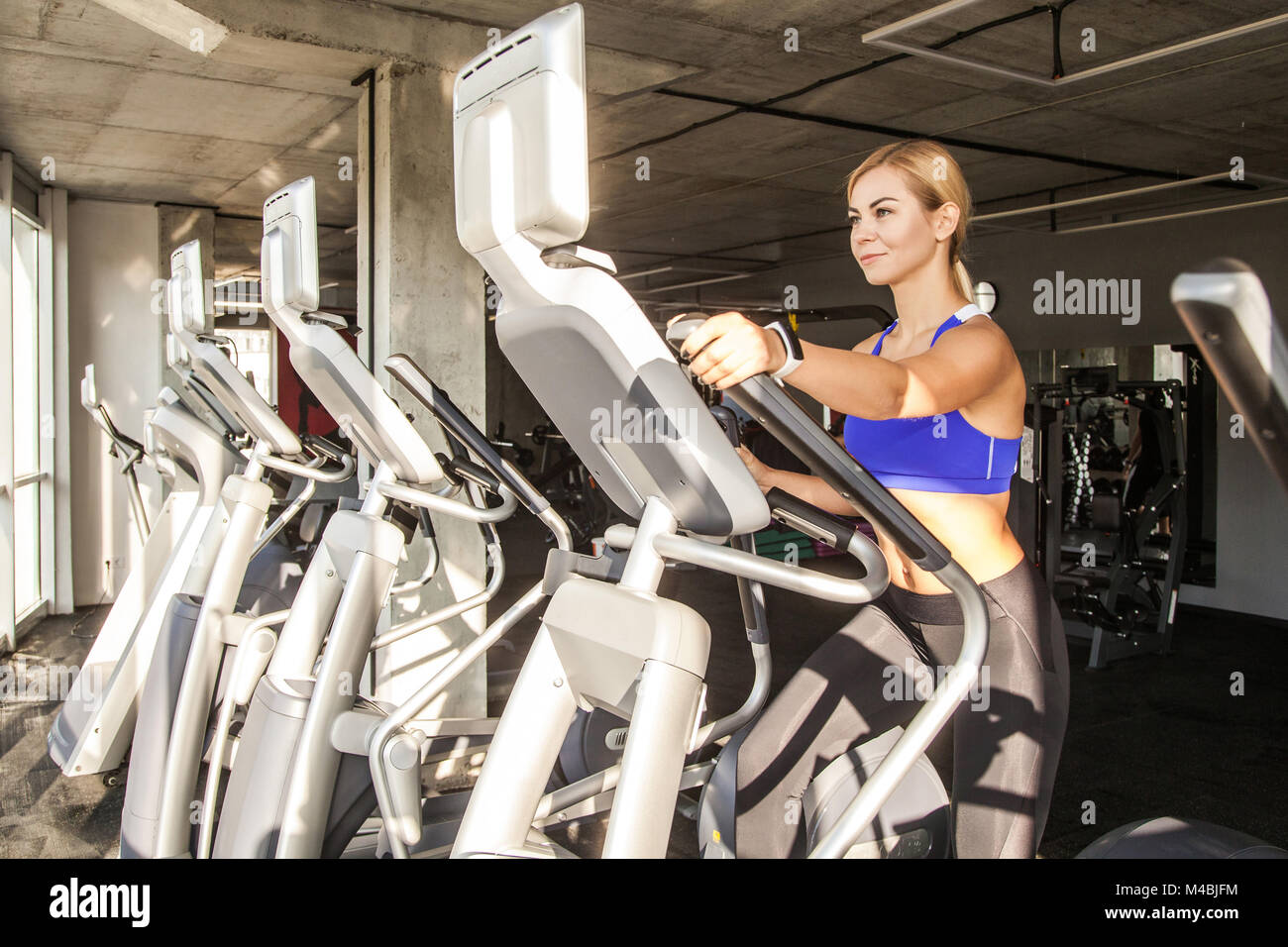 Istruttore donna bionda nel fitness club, ride su orbitrack. Studio shot Foto Stock
