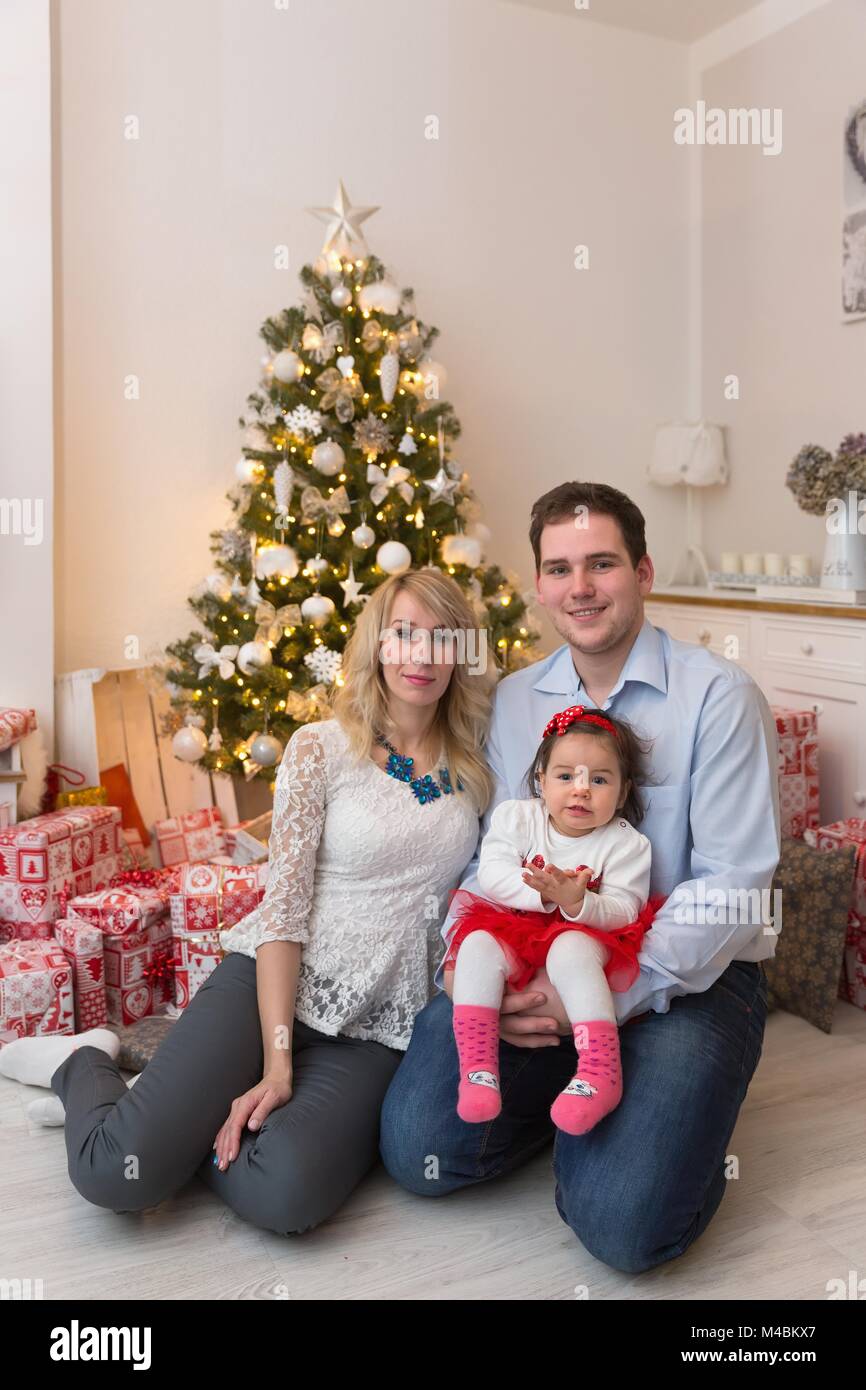 Giovane famiglia felice nella parte anteriore di un albero di Natale Foto Stock