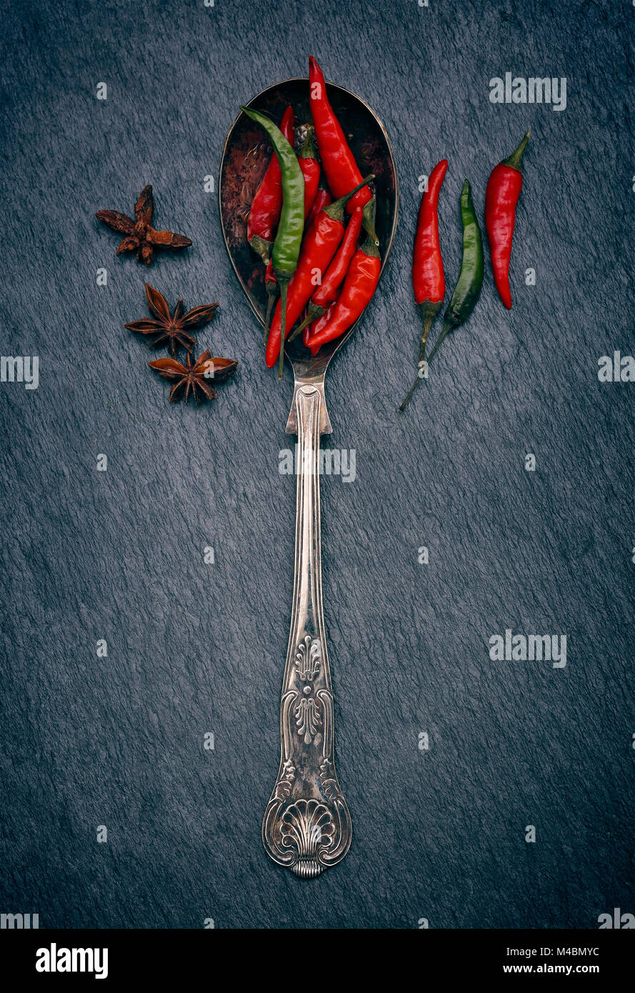 Rosso e peperoncini verdi in un cucchiaio su un rustico di ardesia grigia con sfondo spazio copia Foto Stock