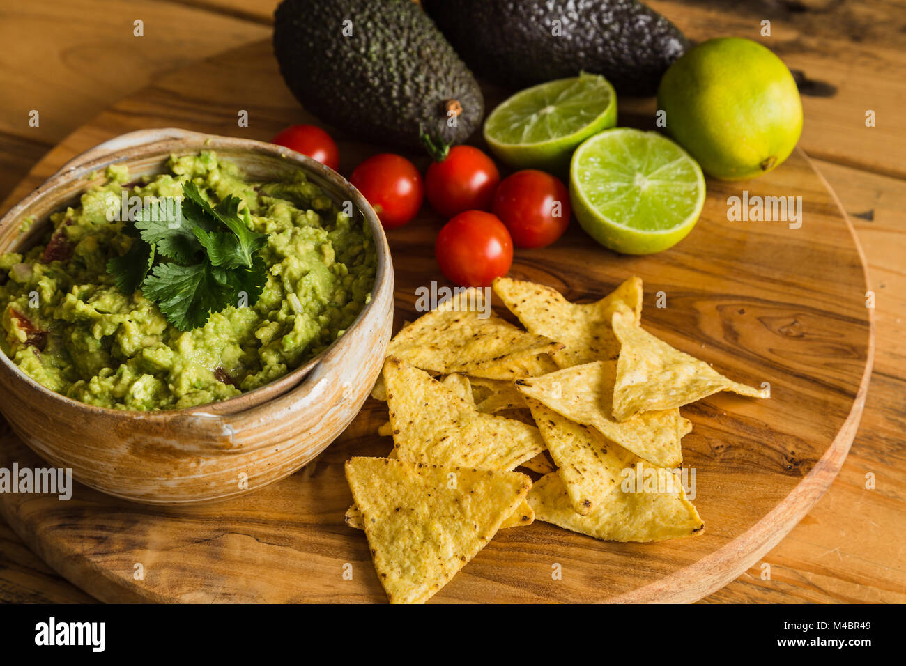 La vaschetta del guacamole dip con gli avocadi tortilla chips di pomodori ciliegini e limes su un tagliere Foto Stock