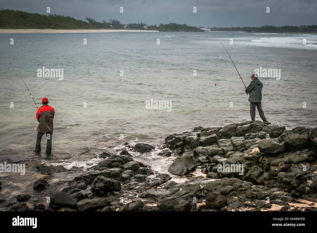 Due uomini di pesca ad angolo su una spiaggia rocciosa di una baia, Mauritius Foto Stock