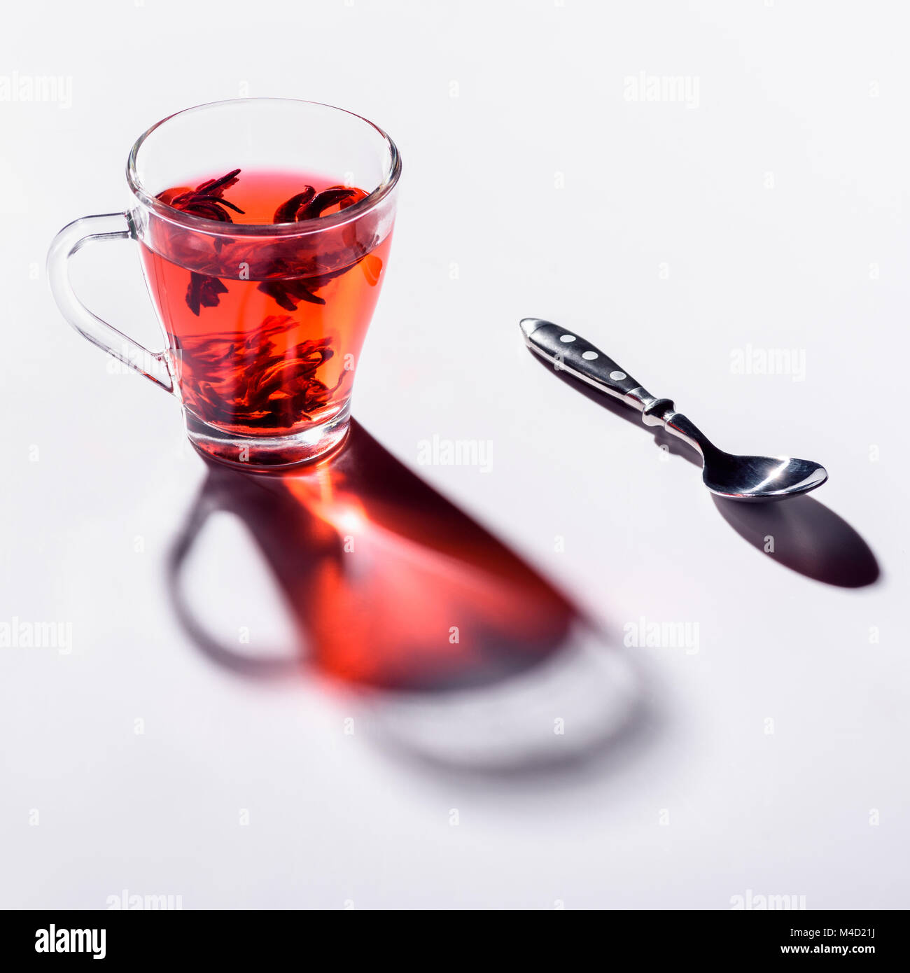 Bicchiere di vetro con tè di ibisco e cucchiaio sul tavolo bianco Foto Stock