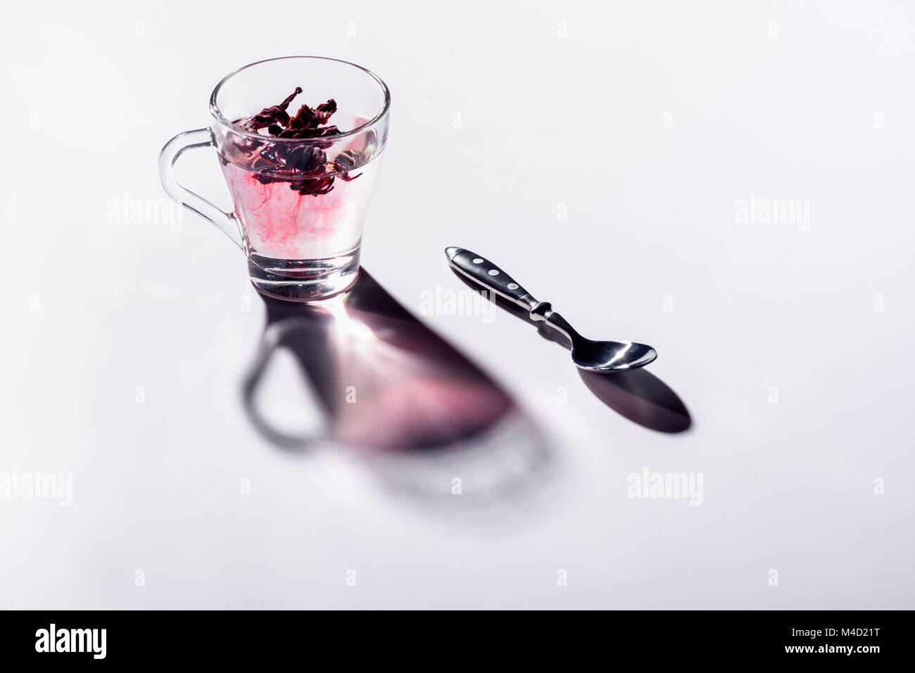 Bicchiere di vetro di hibiscus tè con il cucchiaio sul tavolo bianco Foto Stock