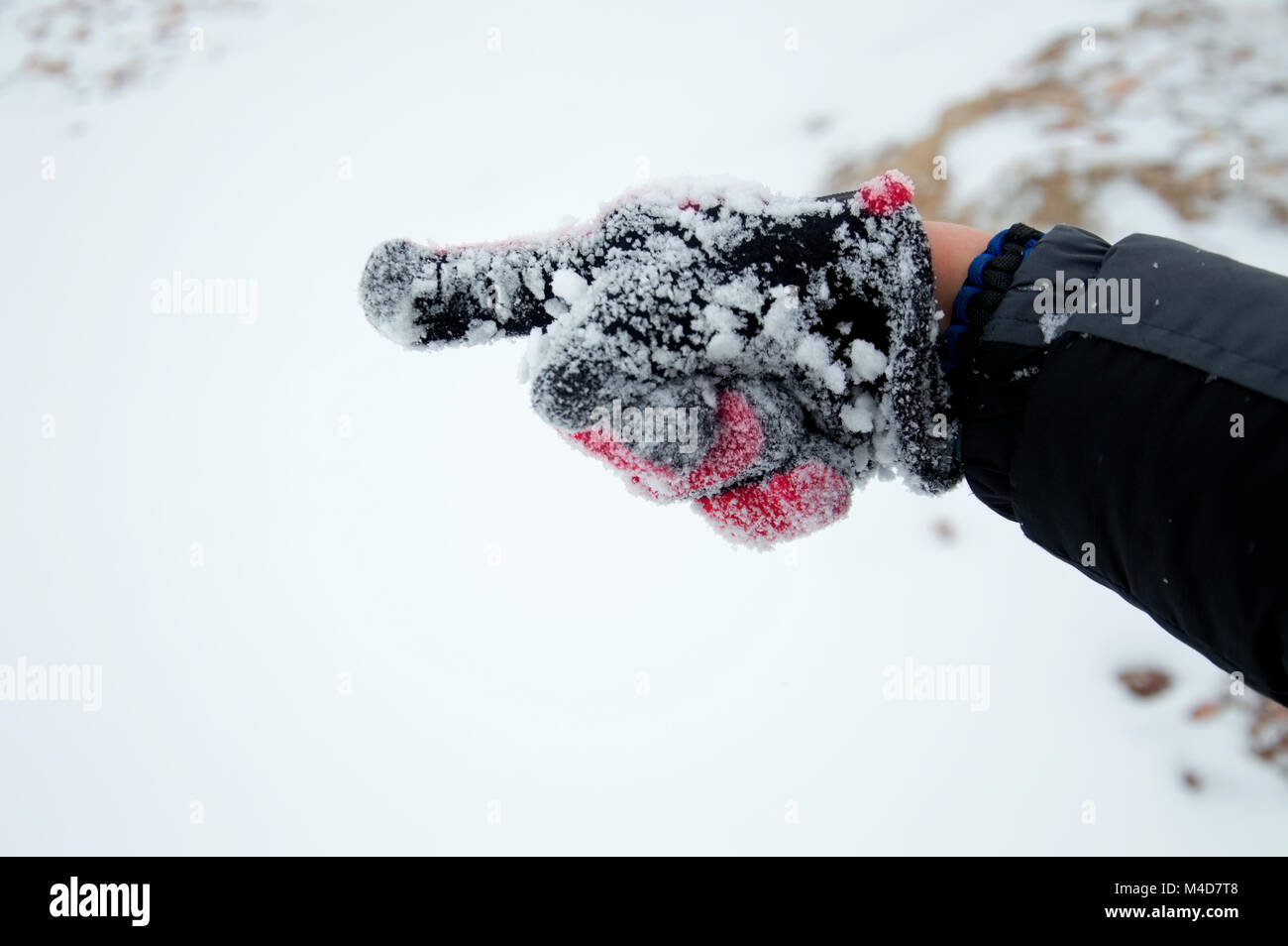 Un rosso mano guantata che mostra una rivolta verso la neve. Foto Stock