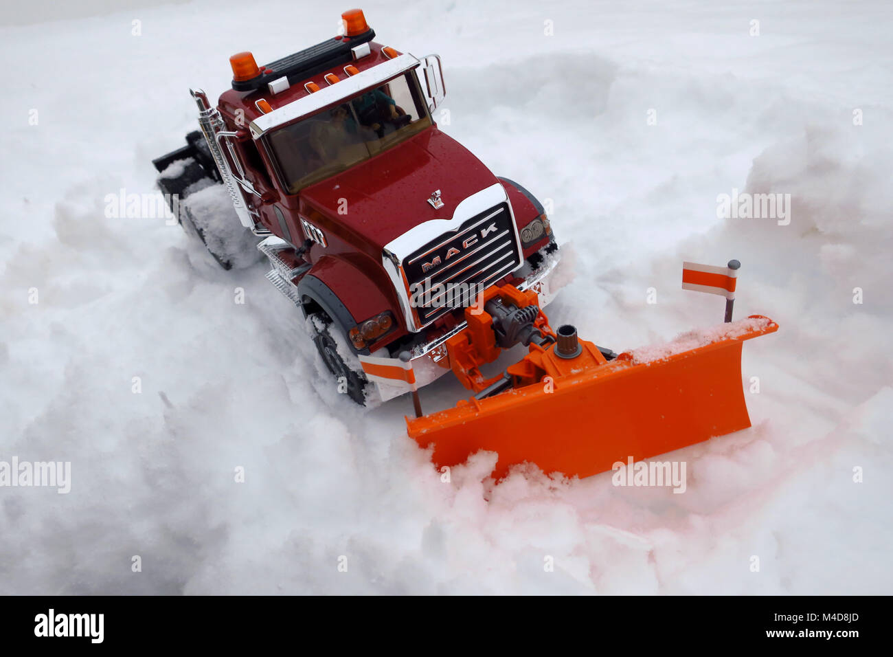 Un giocattolo rosso semi carrello con un arancione spartineve arando un cumulo di neve. Foto Stock