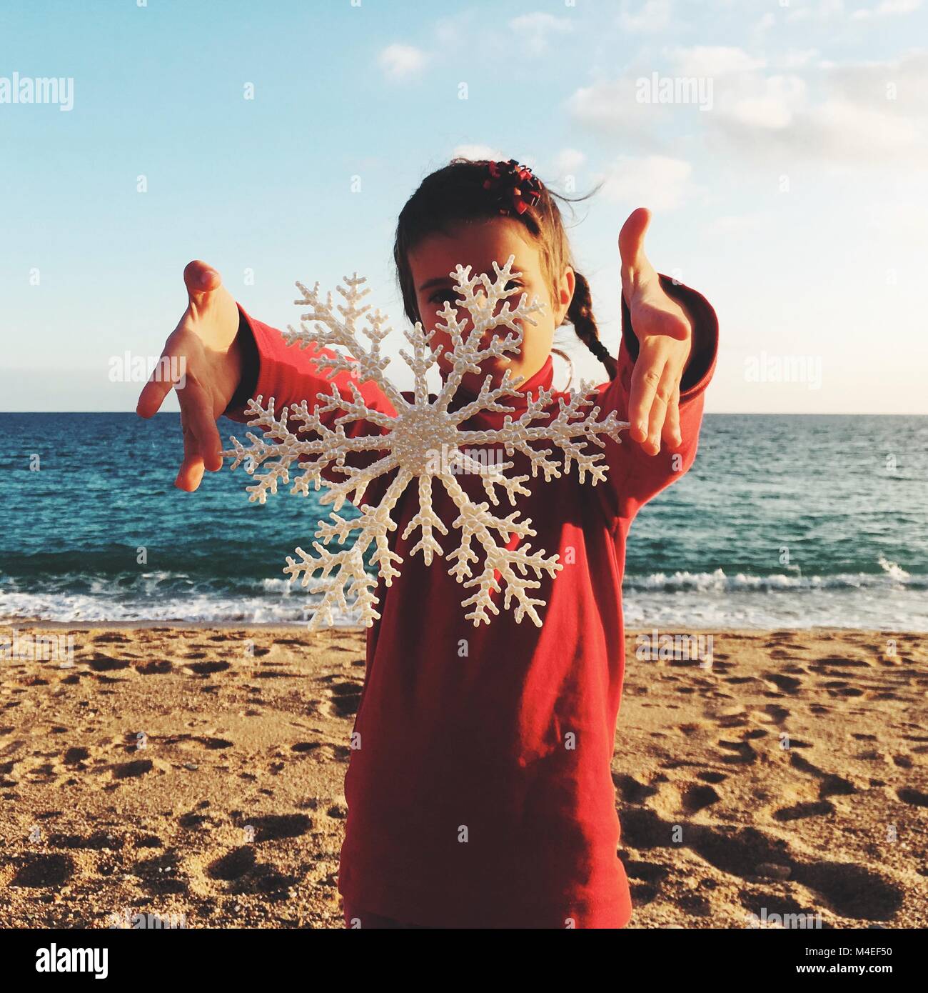 Ragazza in piedi sulla spiaggia tenendo un natale decorazione a fiocco di neve Foto Stock