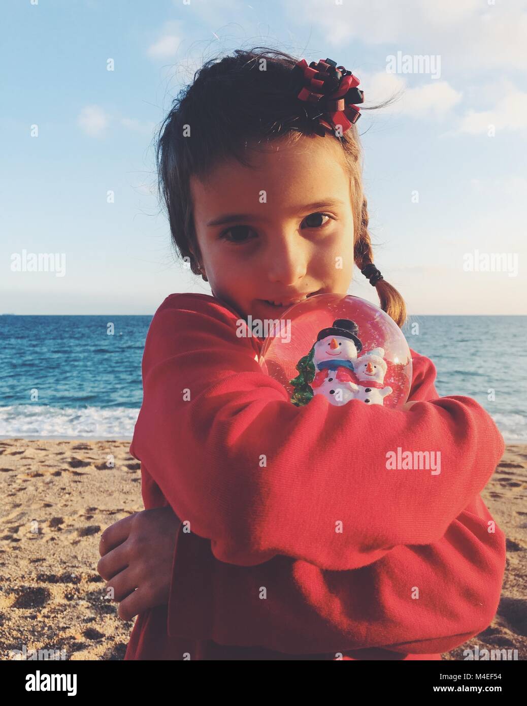 Ragazza in piedi sulla spiaggia che abbraccia un Natale Snow Globe Foto Stock