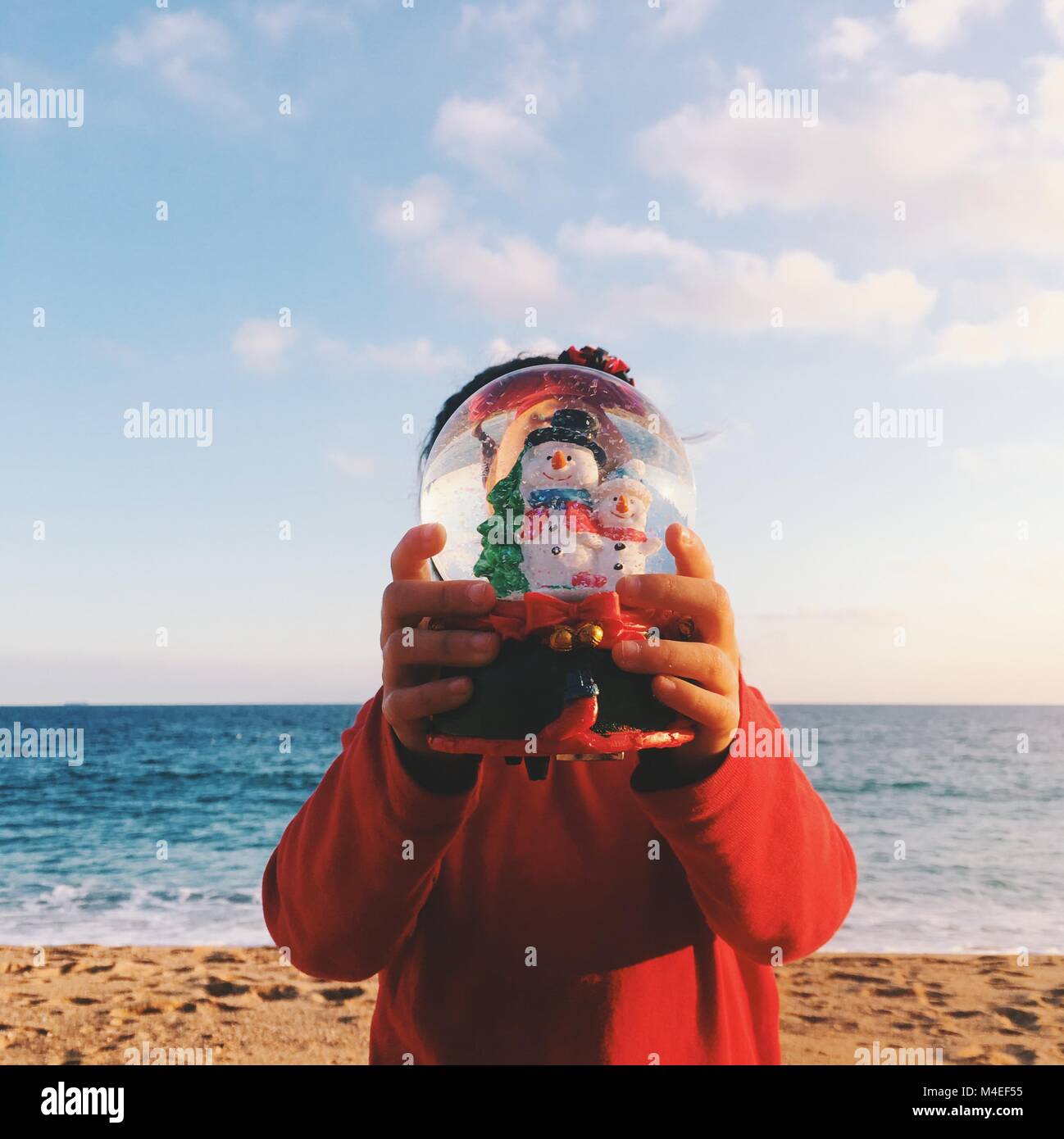 Ragazza in piedi sulla spiaggia tenendo un Natale Snow Globe Foto Stock
