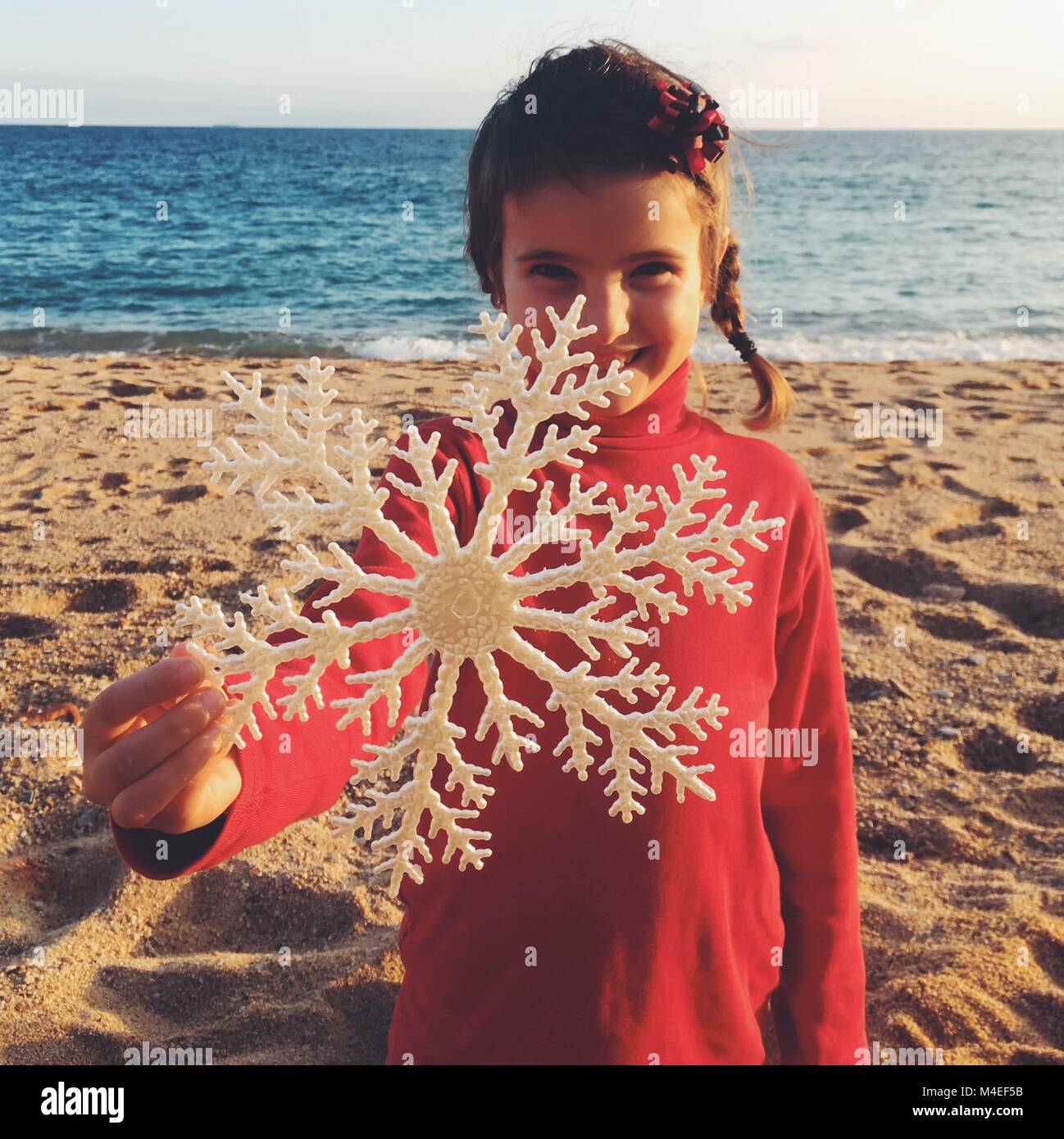 Ragazza in piedi sulla spiaggia tenendo un natale decorazione a fiocco di neve Foto Stock