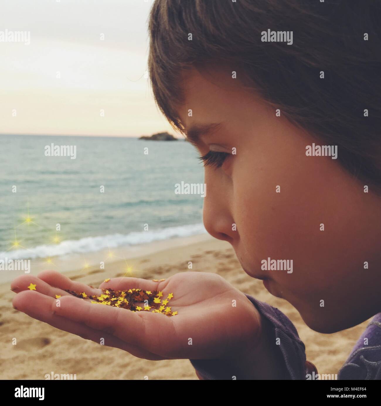 Ragazza in piedi sulla spiaggia a soffiare una manciata di oro coriandoli stelle Foto Stock