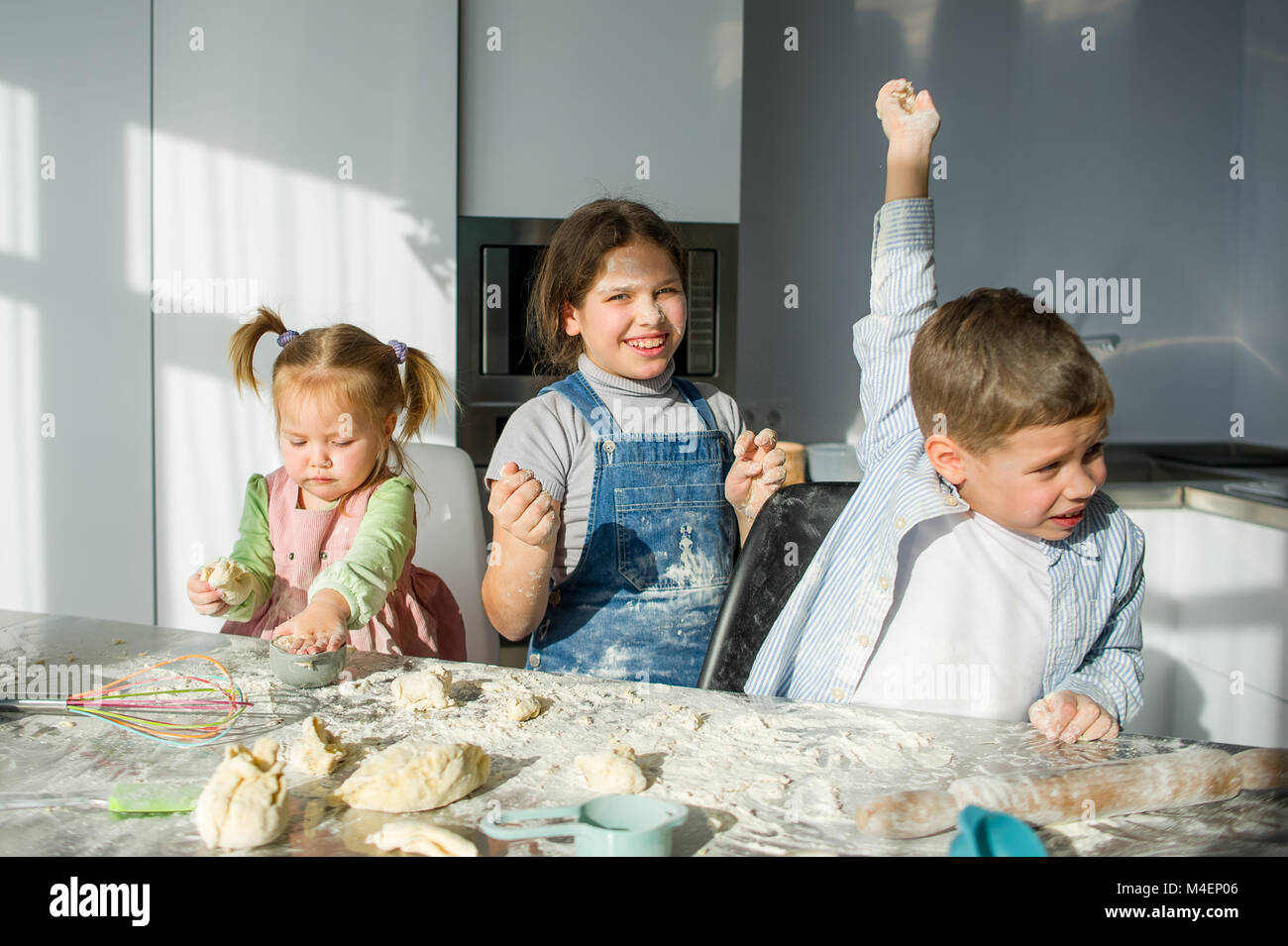 Tre bambini preparare qualcosa dall'impasto. Due sorelle e un fratello sono seduti al tavolo della cucina. Ci sono vari utensili di cucina sul Foto Stock